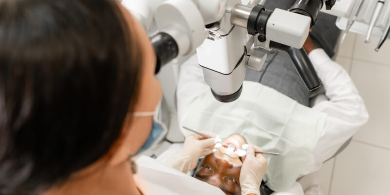 dentist treating root canals using microscope in the dental clinic. Man lying on dentist chair with open mouth