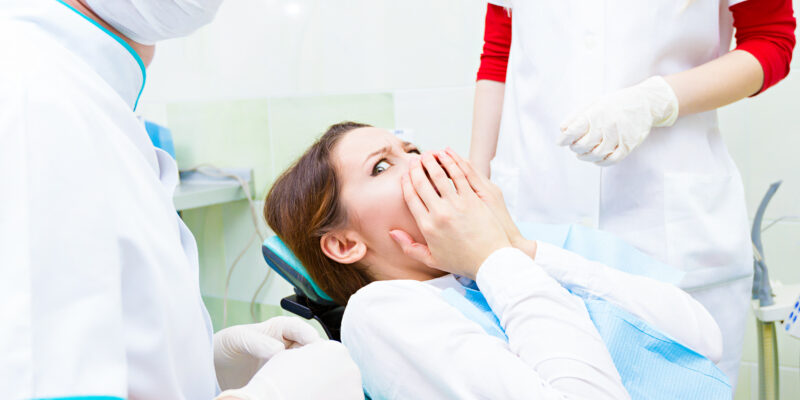 Closeup portrait young terrified girl woman scared at dentist visit, siting in chair, covering her mouth, doesn't want dental procedure