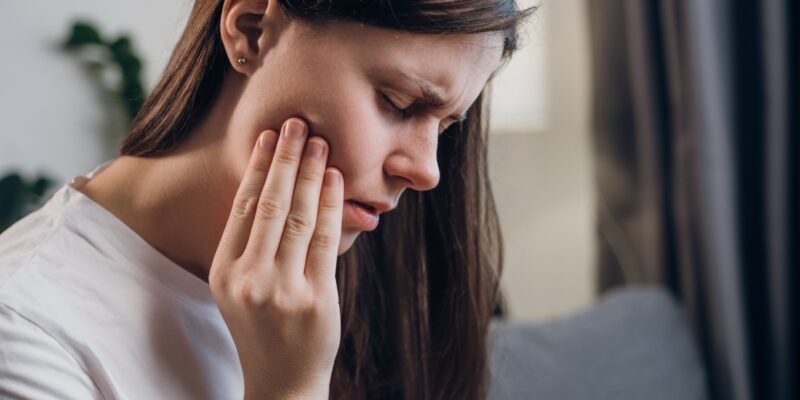 Close up of upset young female 20s touching mouth with hand, painful expression because dental issue.