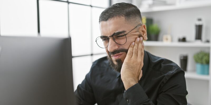 man sitting at his computer with hand on jaw, severe tooth pain